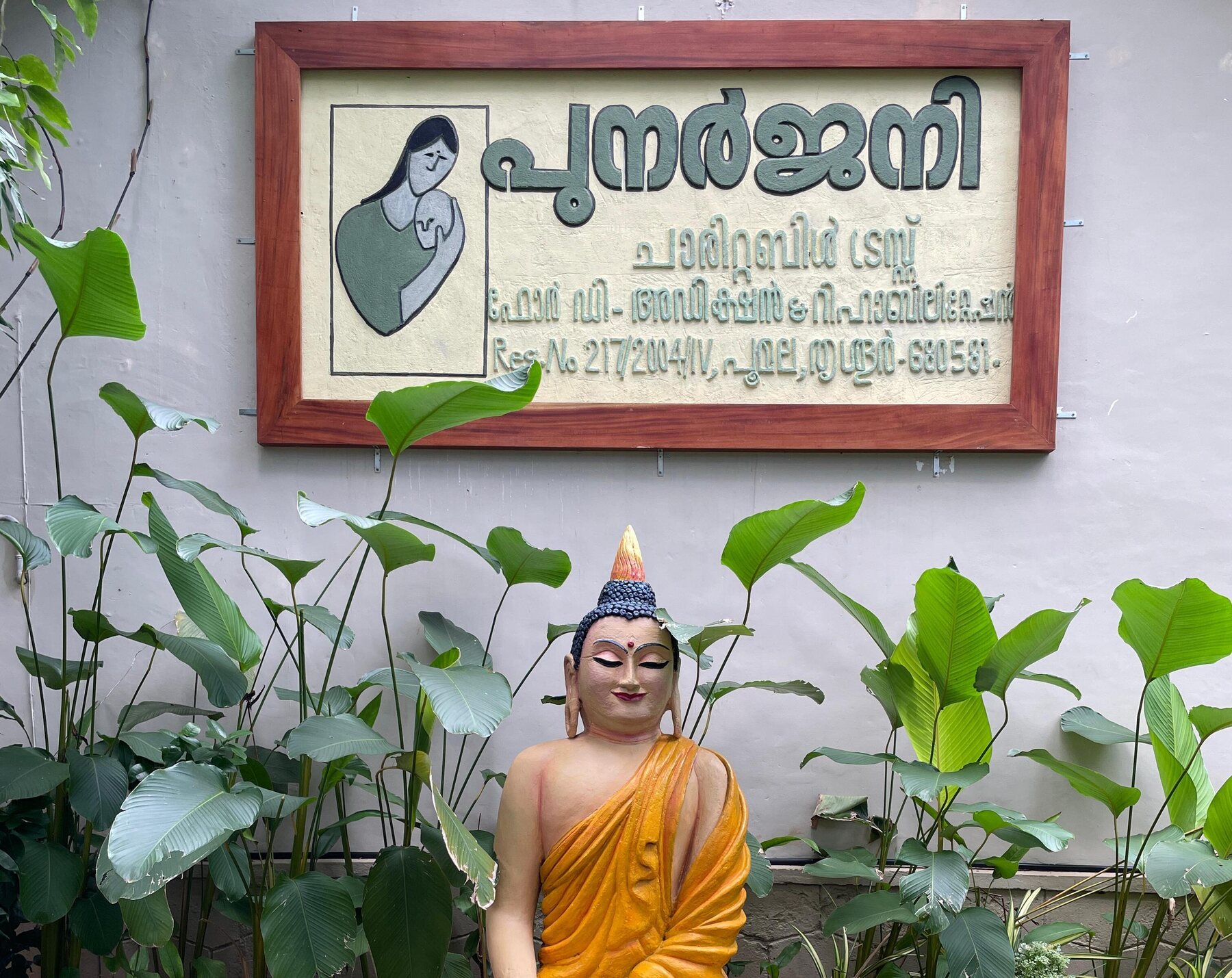 The Punarjjany Charitable Trust signboard above a serene Buddha statue in the campus garden at Poomala